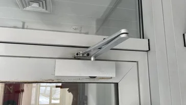 Специалист закрепляет доводчик на верхней части двери.