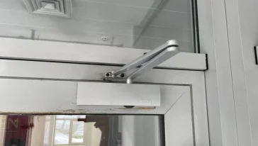 Специалист закрепляет доводчик на верхней части двери.