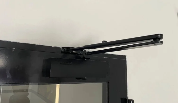 Мастер меняет доводчик на алюминиевой двери.