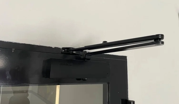 Мастер меняет доводчик на алюминиевой двери.